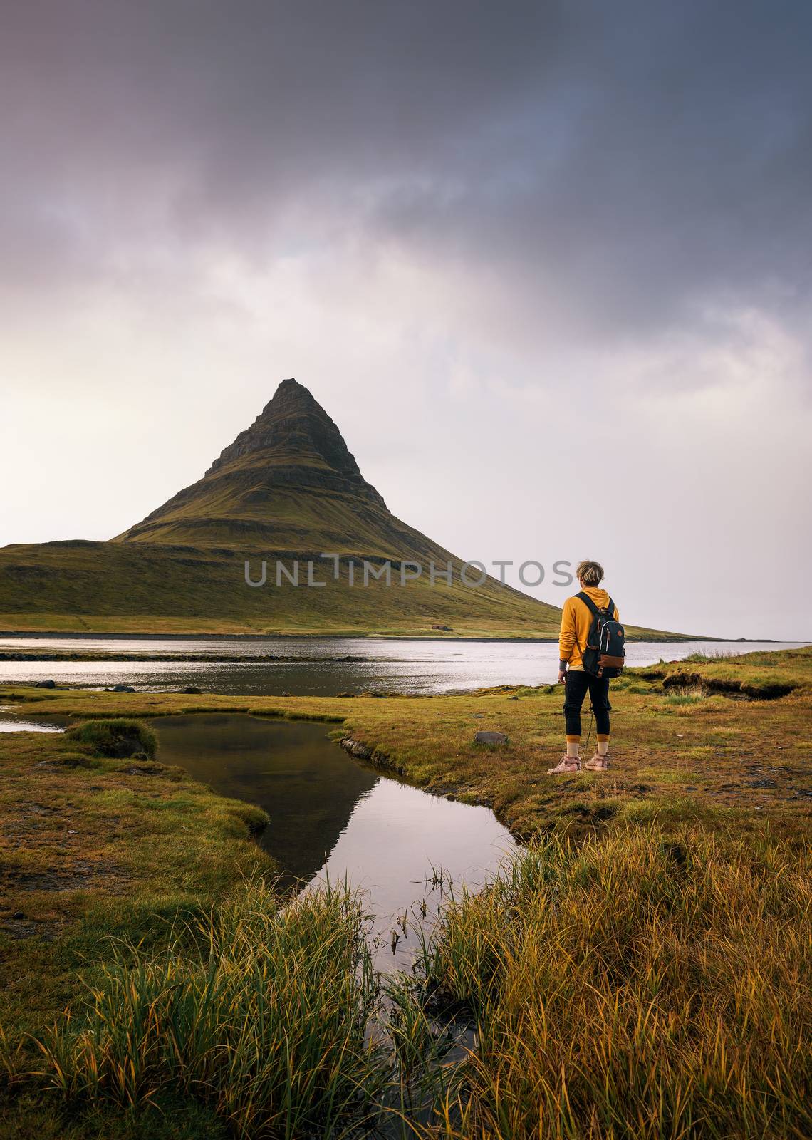Young hiker with a backpack looks at the Kirkjufell mountain in Iceland by nickfox