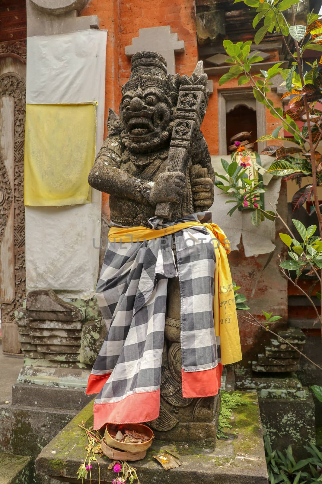 A bricked entrance gate to a Hindu temple on Bali, Indonesia. Entrance gate is closed. There is guardian figure next to it, wrapped in checked material tied with yellow ribbon. A close up.