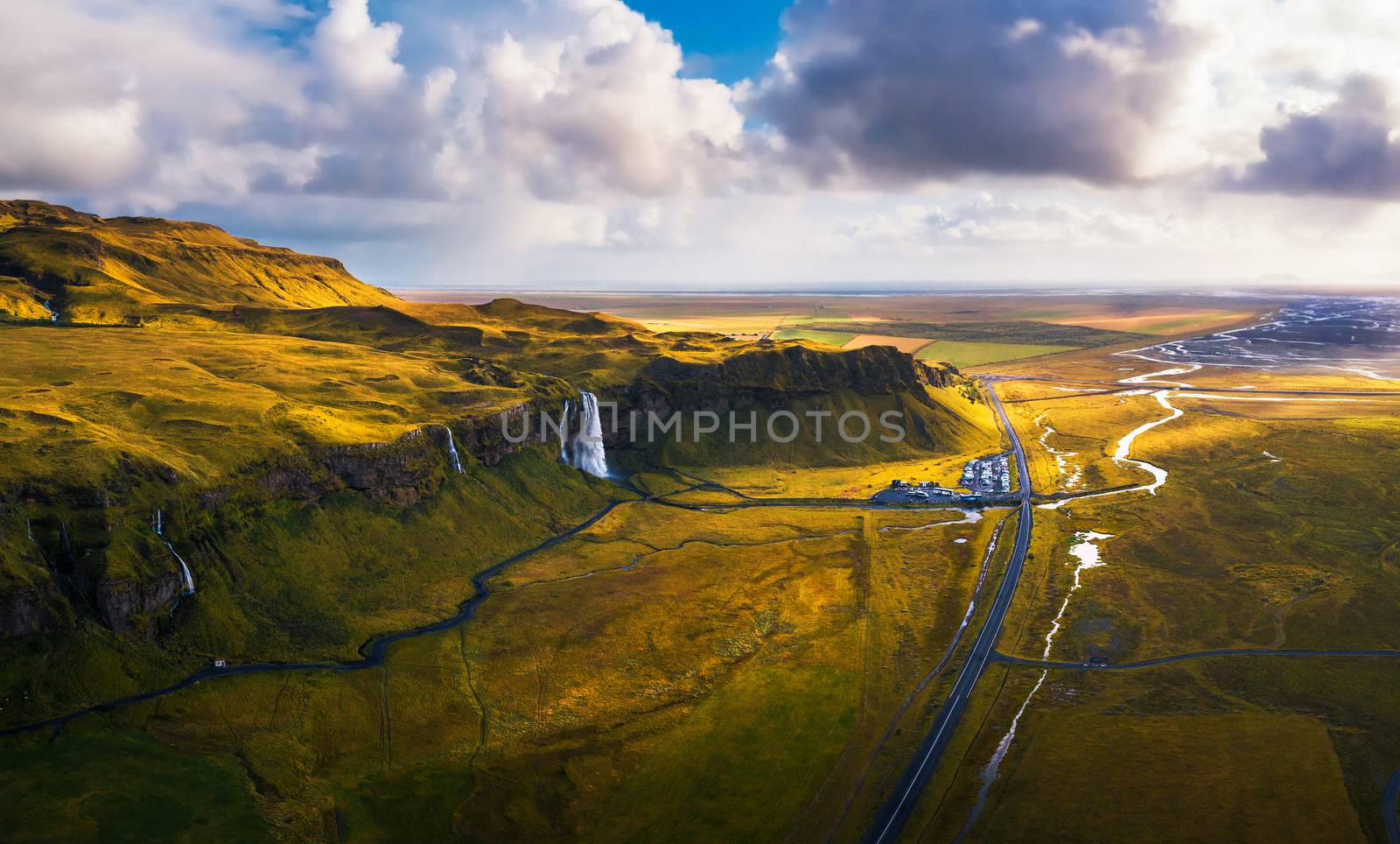 Aerial view of Seljalandsfoss Waterfall, Seljalands River, waterfall parking and the ring road in Iceland at sunset.