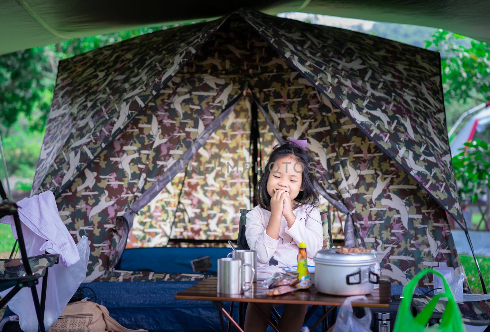 little asian girl sitting and eating breakfast in front of tent while going to camping.The concept of outdoor activities and adventures in nature