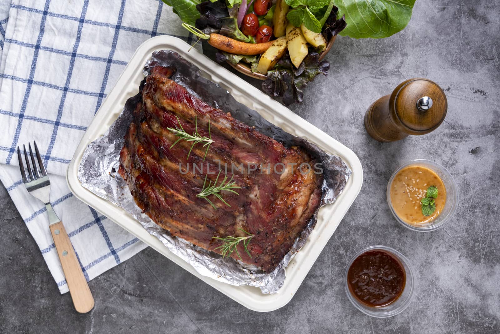 Closeup of pork ribs grilled with BBQ sauce and caramelized in honey with Vegetables and sauces on a drak table, prepared food.