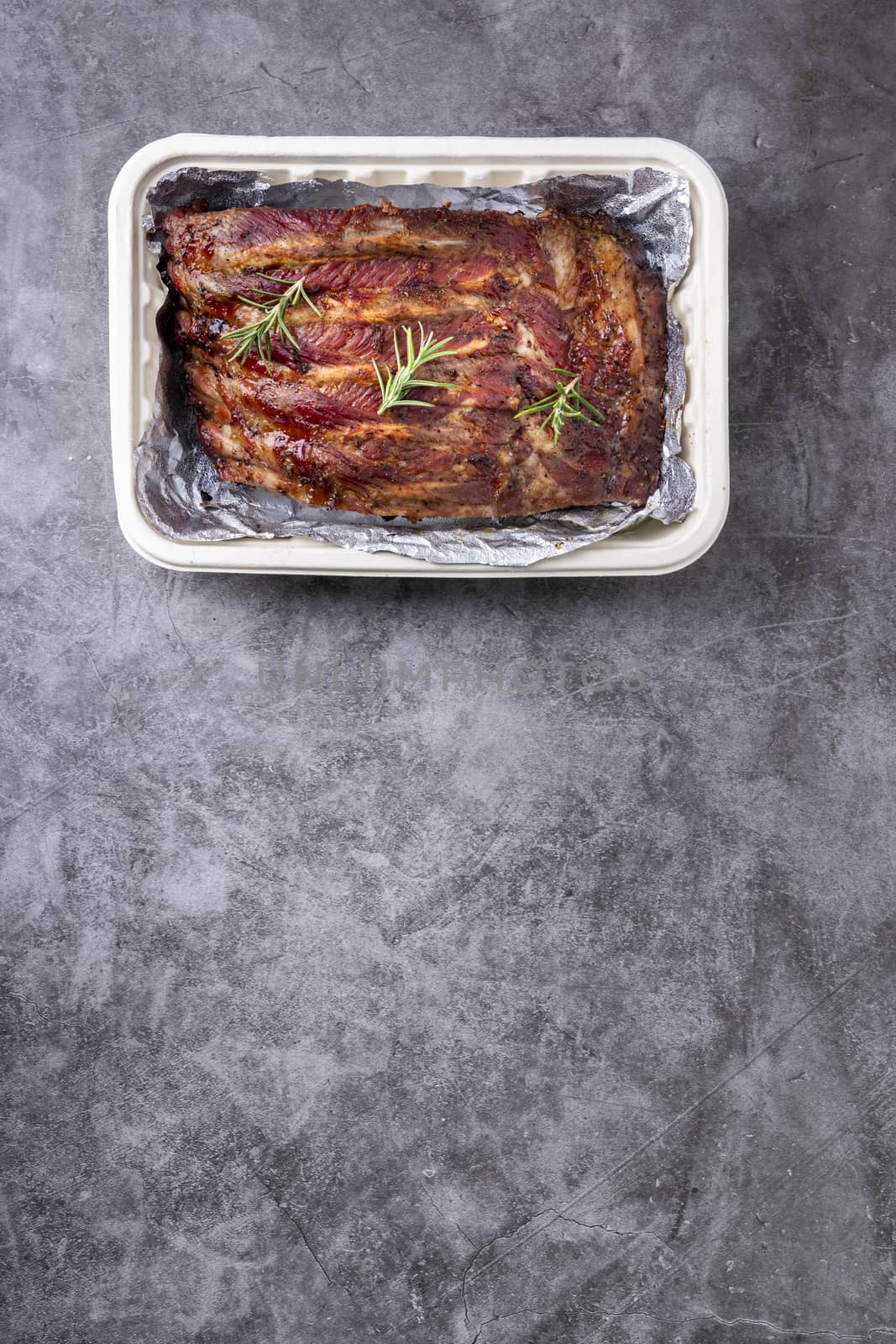 Closeup of pork ribs grilled with BBQ sauce and caramelized in honey with Vegetables and sauces on a drak table, prepared food.