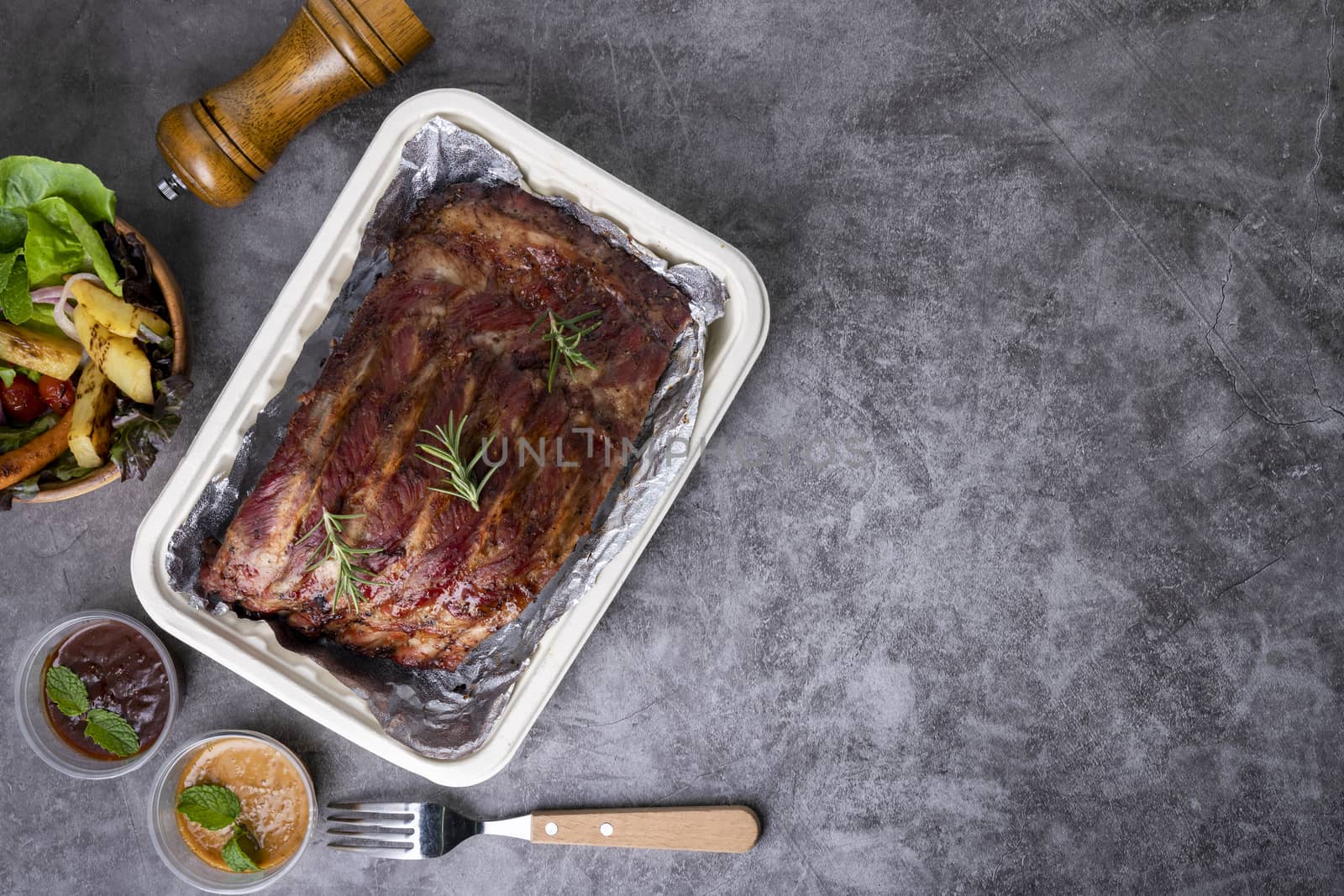 Grilled pork ribs with Vegetables and sauces on a drak table.