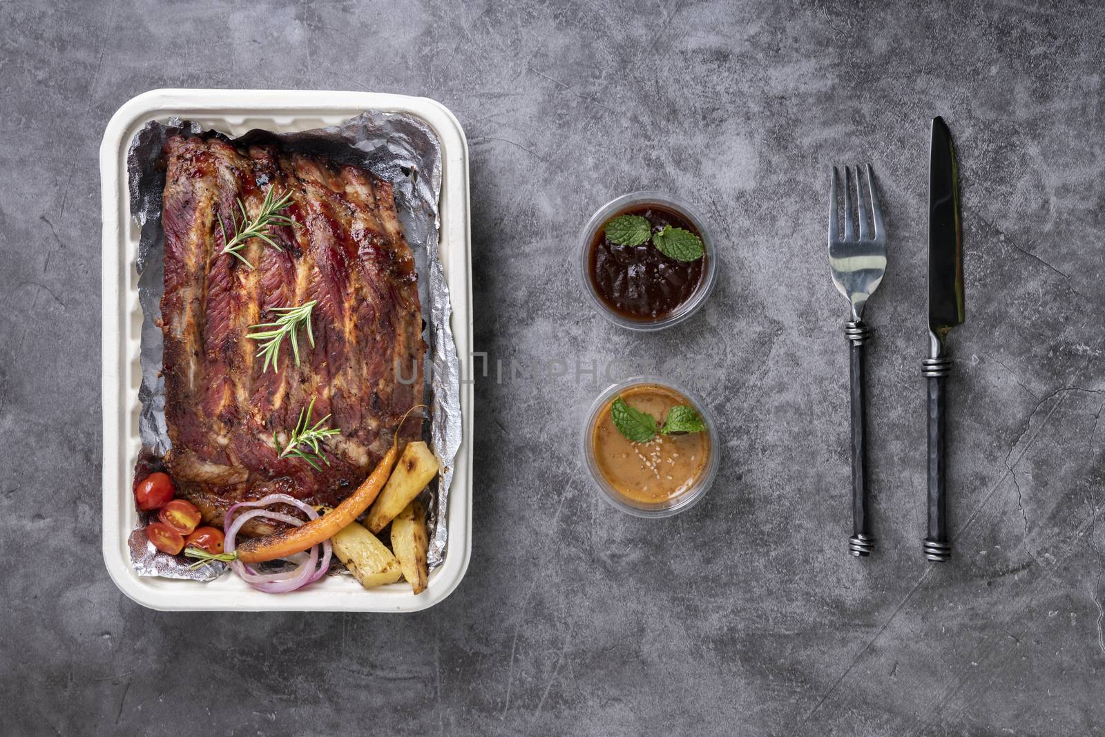 Closeup of pork ribs grilled with BBQ sauce and caramelized in honey with Vegetables and sauces on a drak table, prepared food.