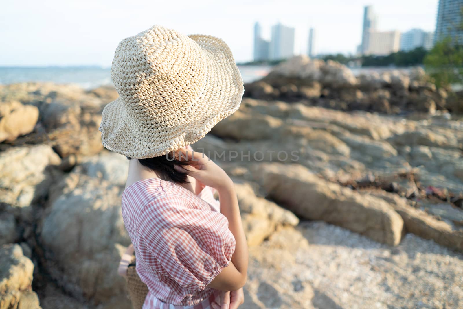 Back view of young woman sitting on the rock at the beach