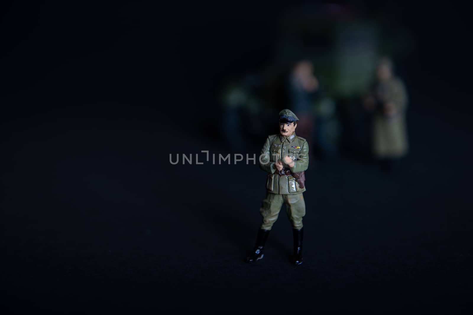 A figure of a man in a military German uniform. In the background of a vague truck and two soldiers by marynkin