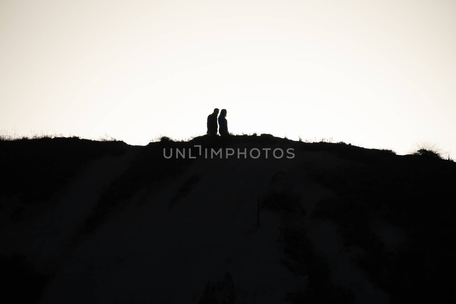 SIlhouette of a couple walking at sunset on a hill.