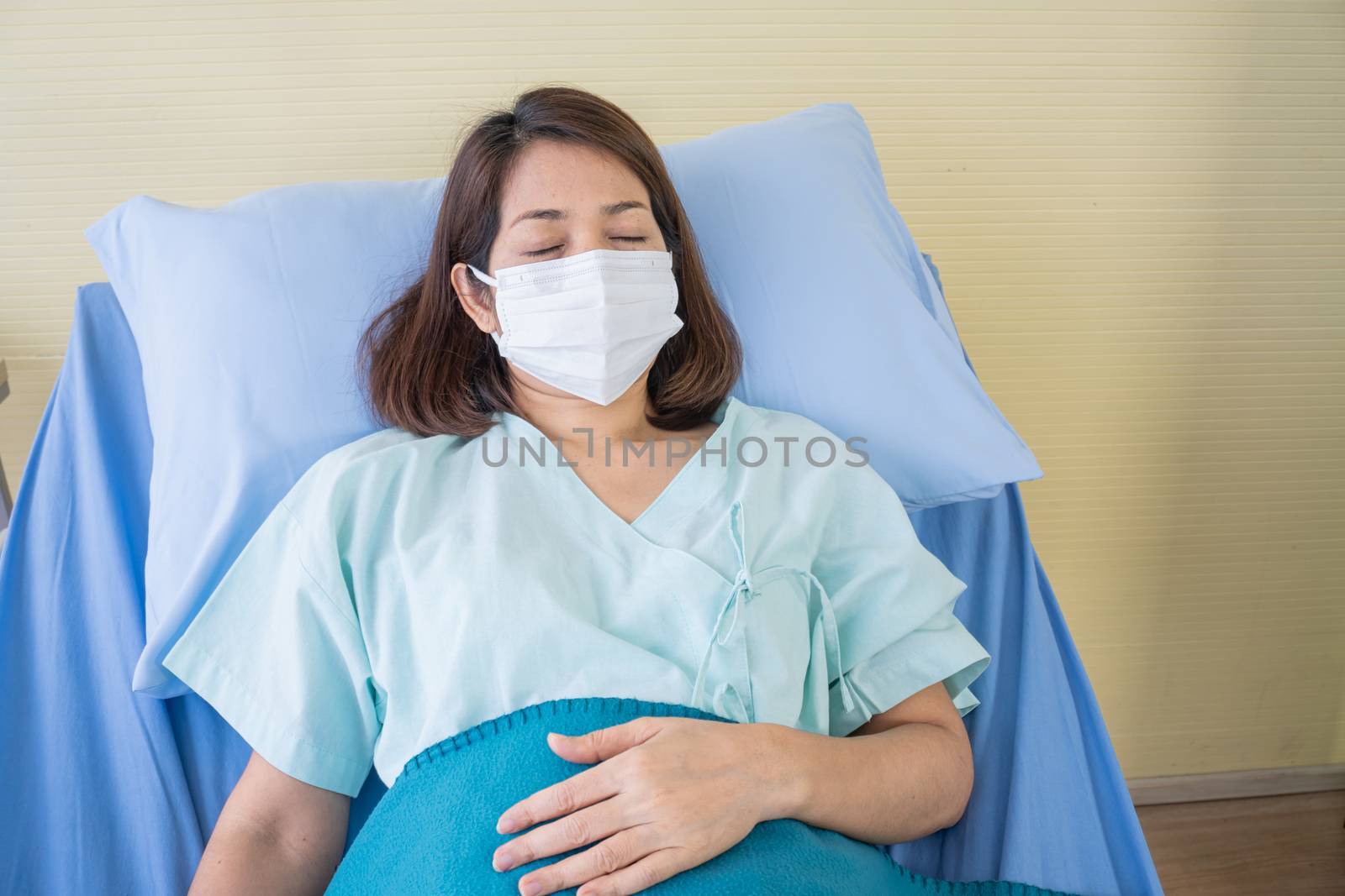 Asian woman is sick has a high fever, sneezing, is recuperating in the patient's dress lay on the patient bed in the hospital with face masks protect virus. covid19 concept
