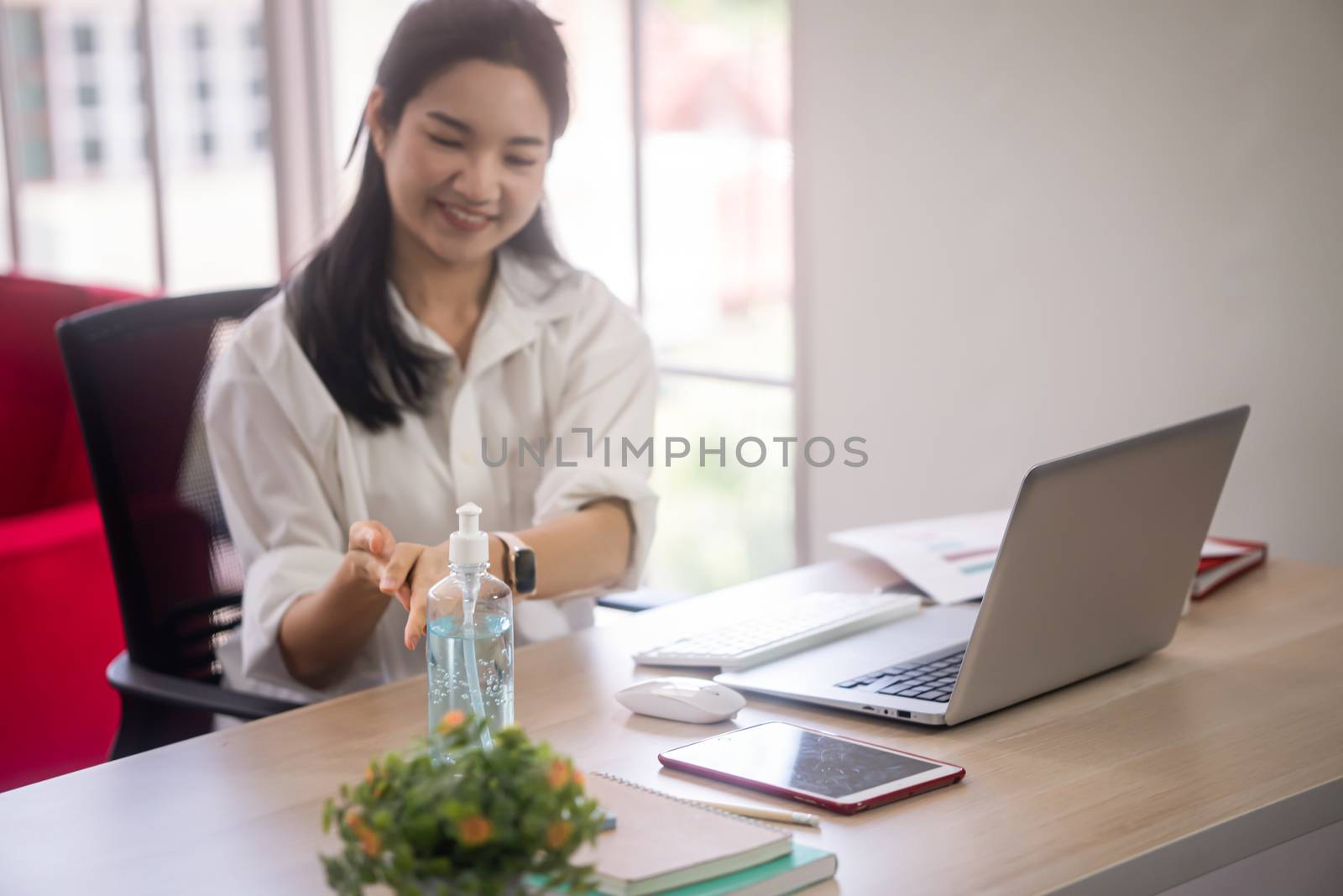 young asian woman clean her hand with alcohol gel to protect covid19 infection from her work space