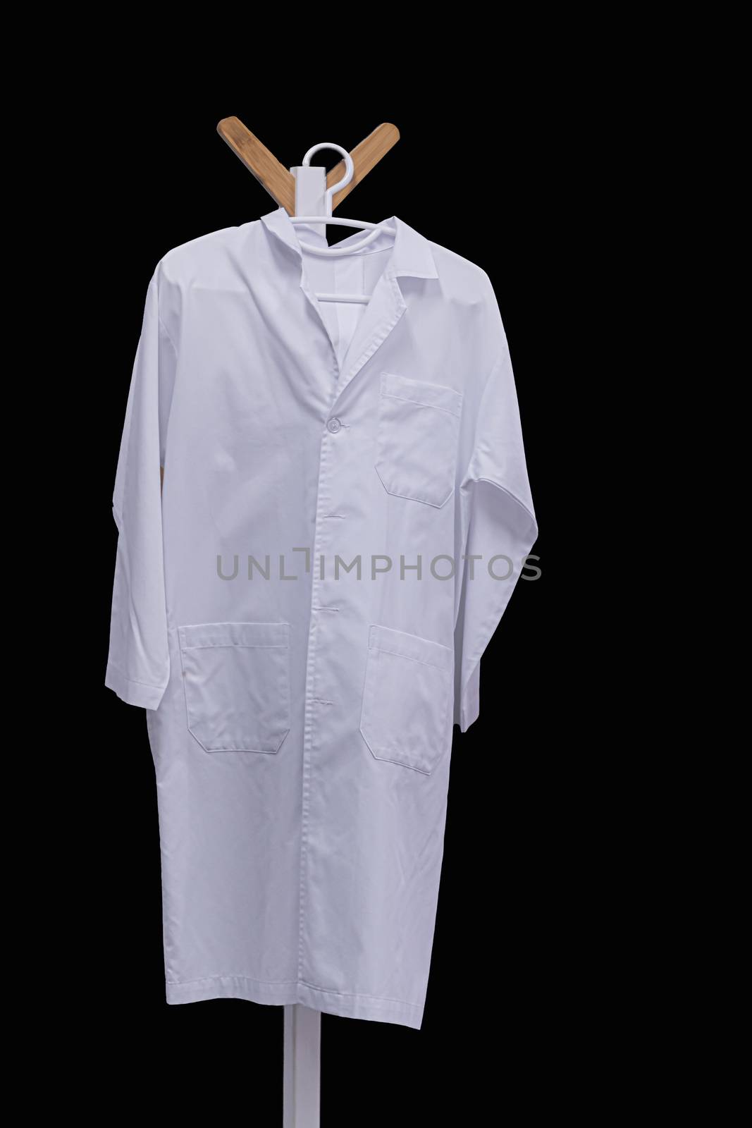 white medical gown hanging on wooden hanger isolated on black background with clipping path by sandyman