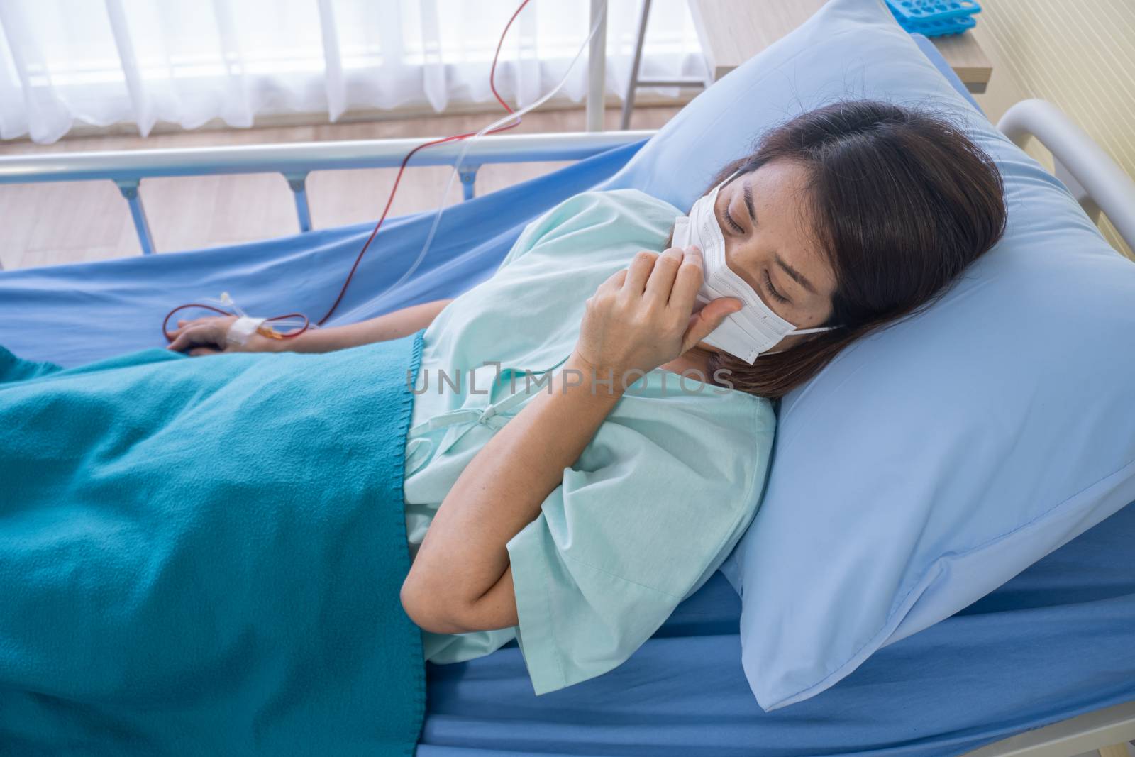 Asian woman is sick has a high fever, sneezing, is recuperating in the patient's dress lay on the patient bed in the hospital with face masks protect virus. covid19 concept