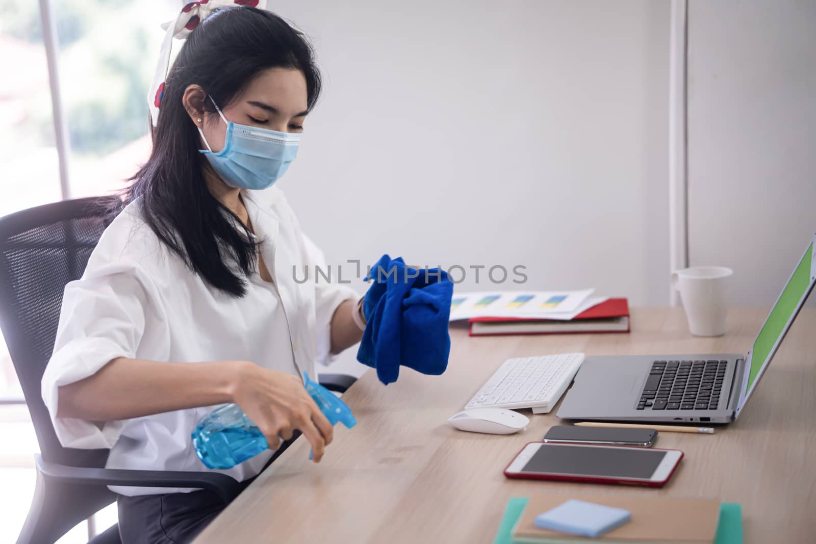 young asian woman cleaning her computer desk and equipment to protect covid19 virus infection