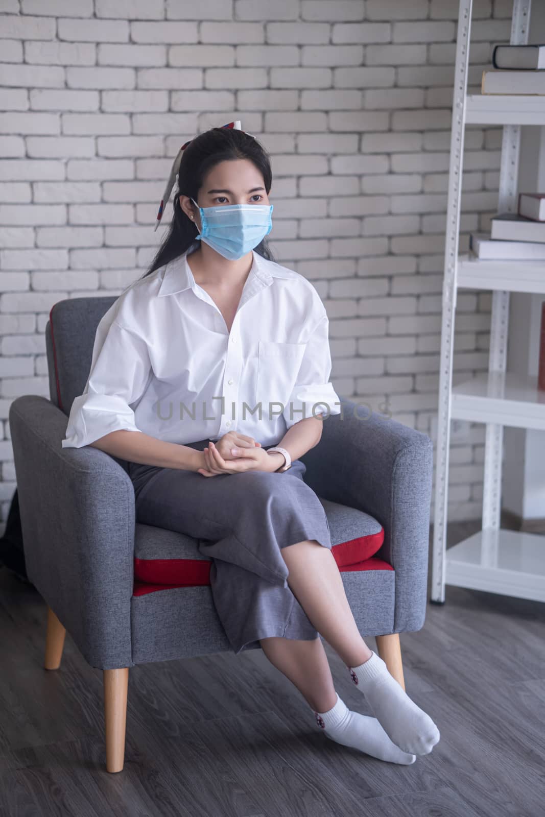 beautiful young asian woman wearing face mask to protect covid19 virus while sitting against white brick wall