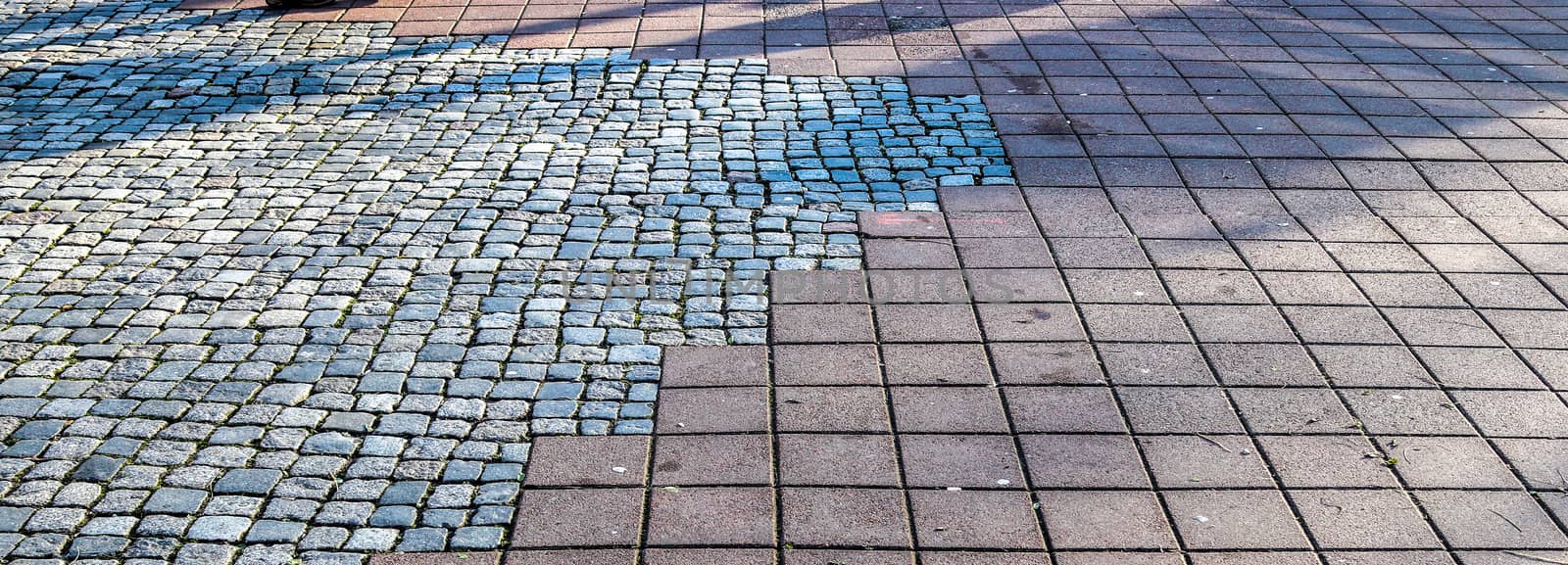 Shadows of people in a shopping area on a cobblestone ground