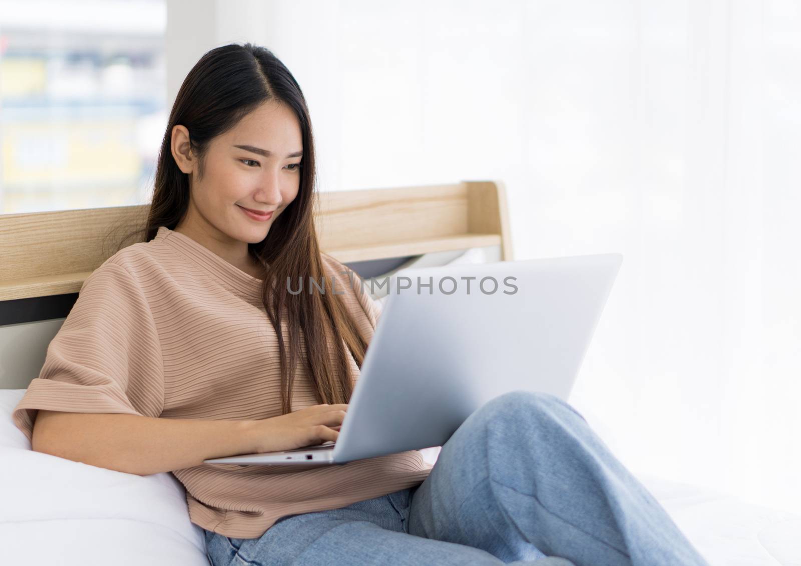 Young asian teen use laptop computer on the bed to relax in the bedroom, enjoy leisure weekend at home. Stress free concept