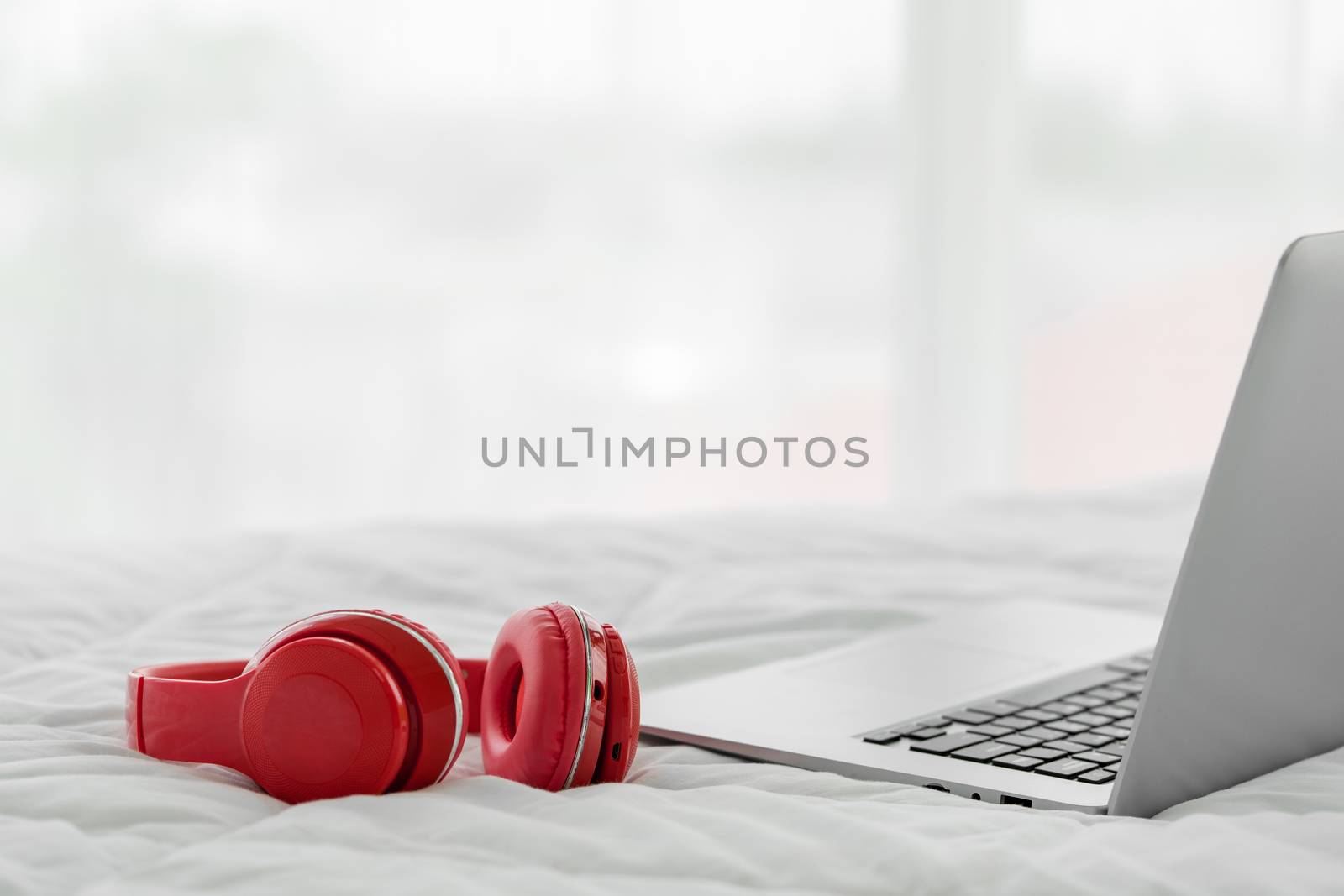 Red modern headphones and laptop computer on white bedsheet. by chadchai_k