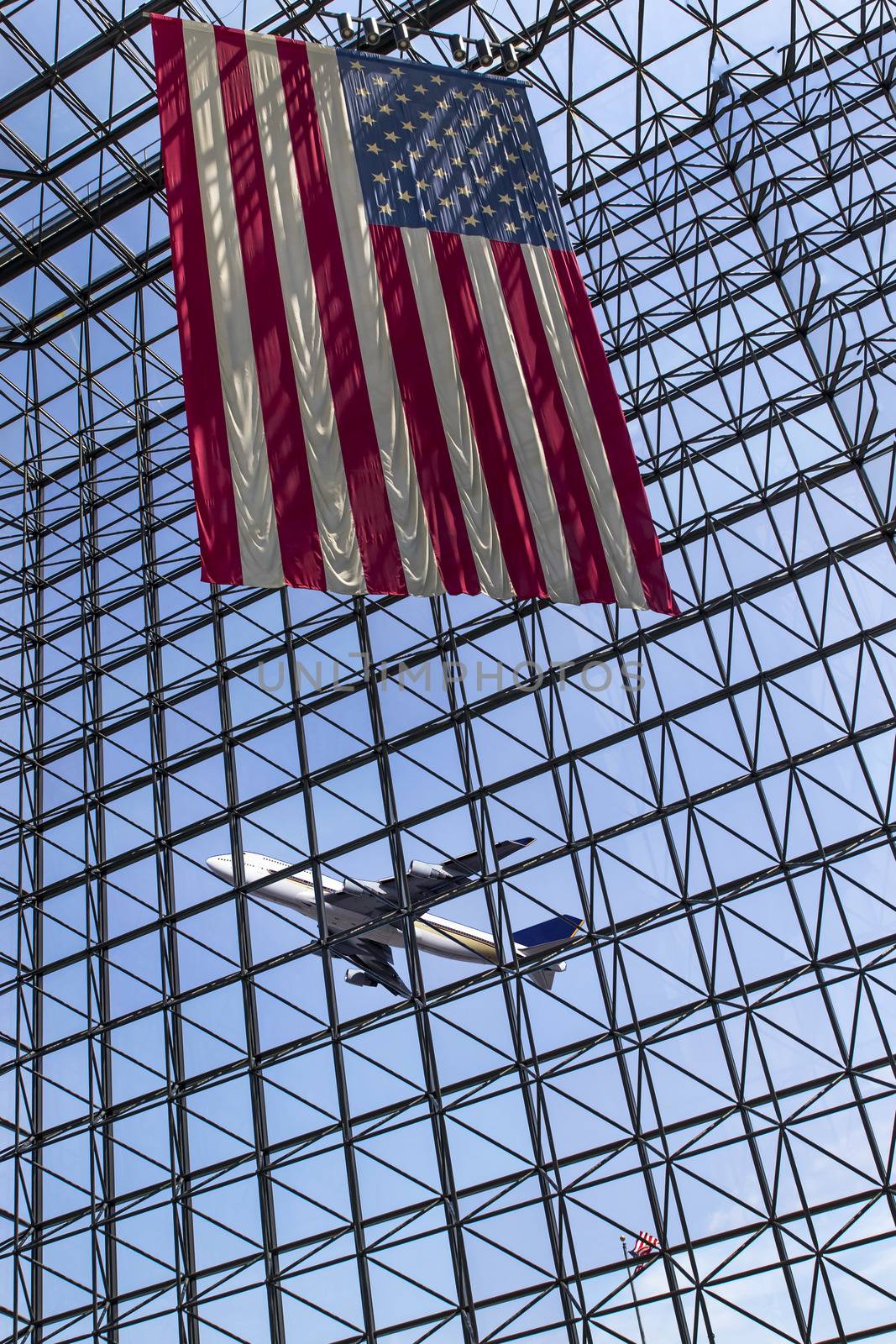 A commercial aircraft takes off from an international airport with an American flag in the foreground