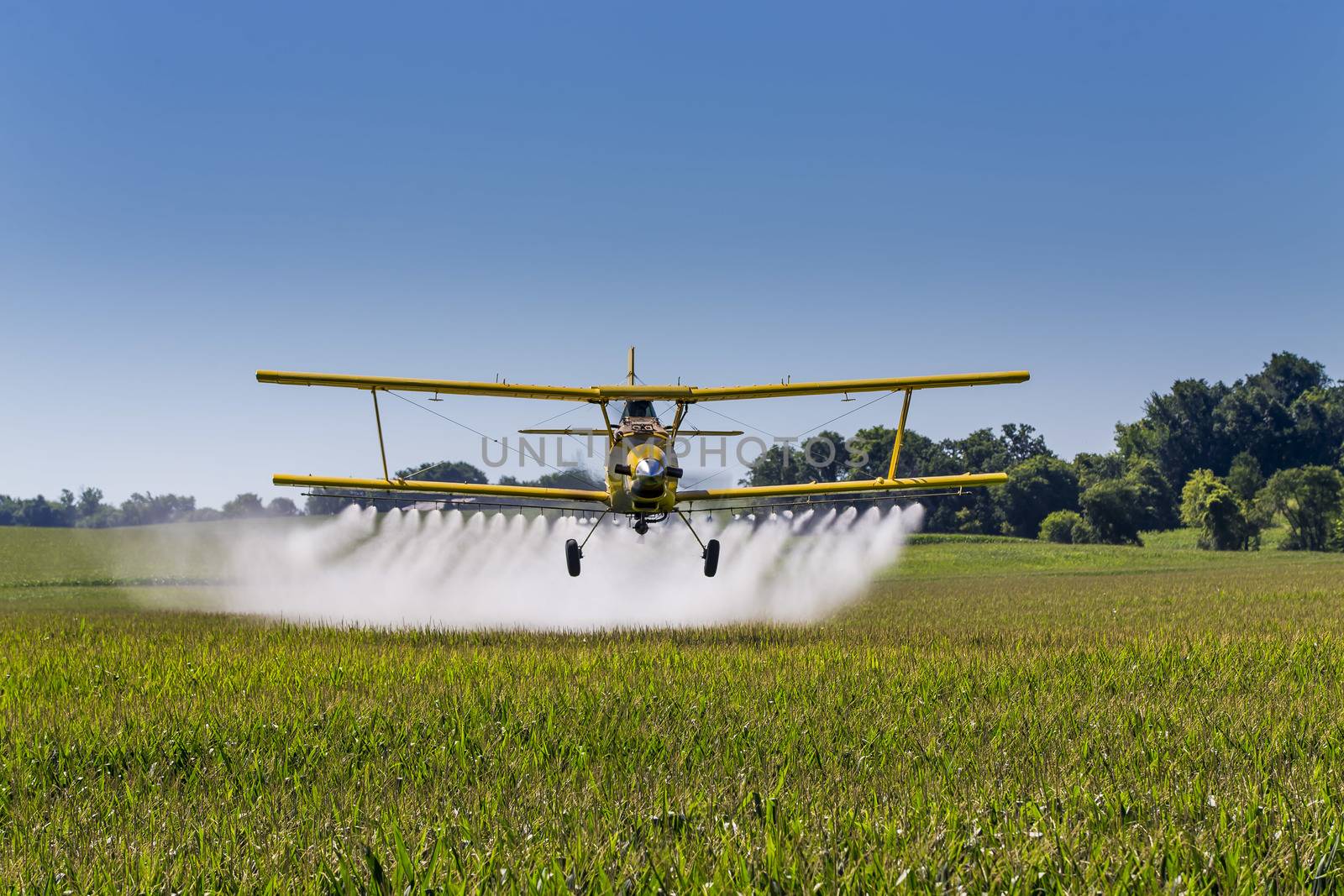 A crop duster applies chemicals to a field of vegetation.