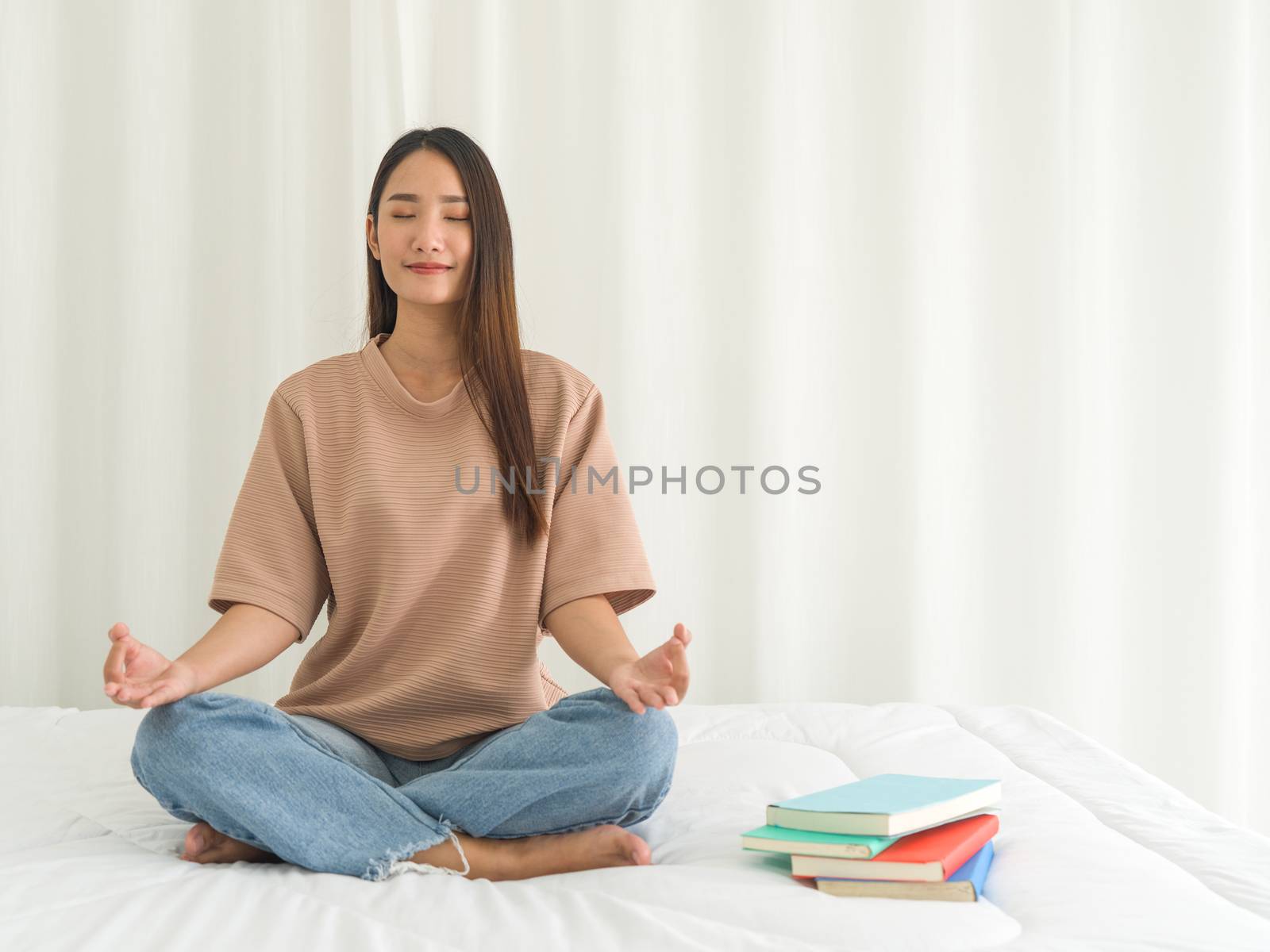 Young woman meditating on bed at home after reviewing the textbook. Morning fitness, mindfulness concept.