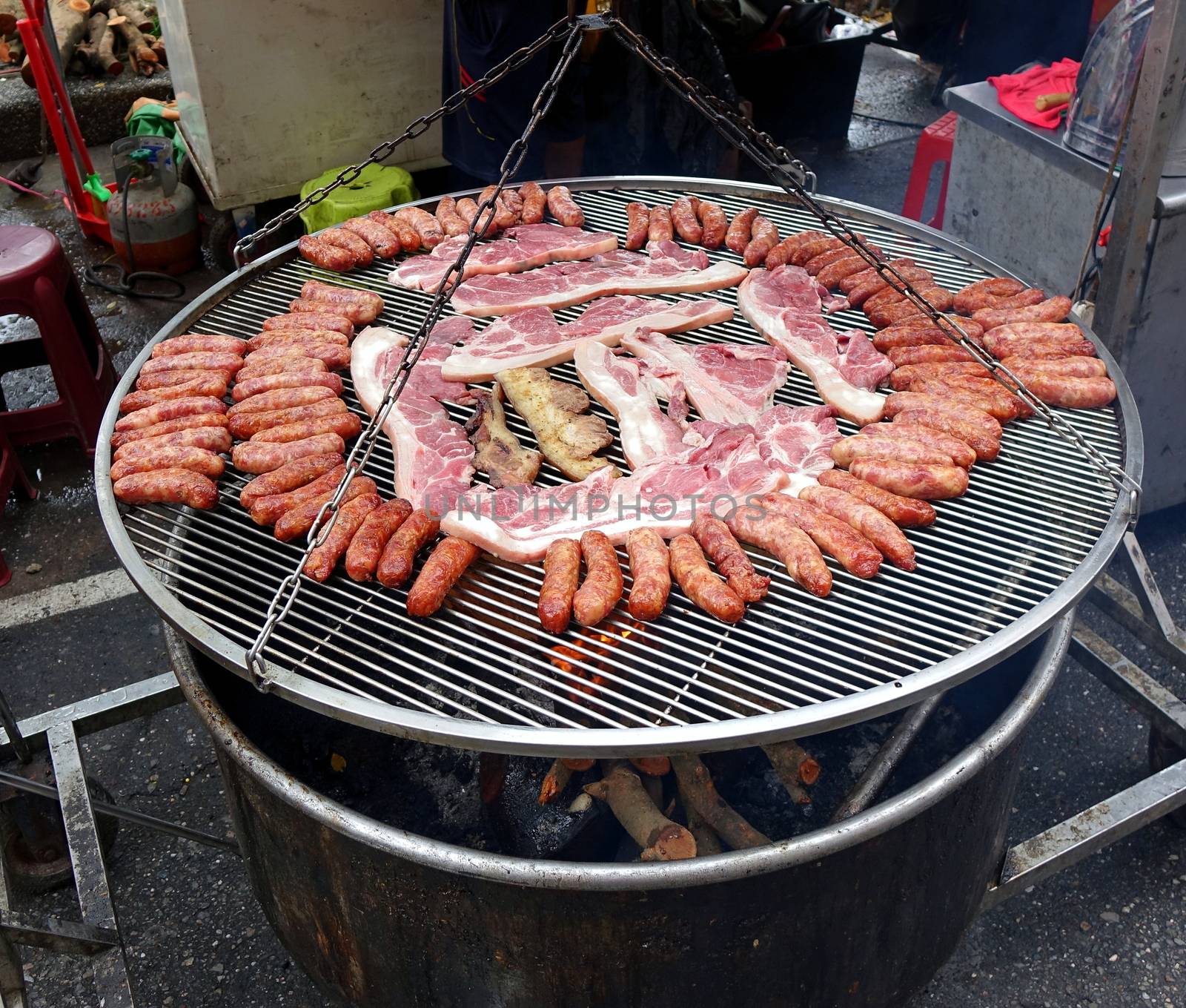 A street vendor cooks sausages and slabs of pork on a large barbecue rack
