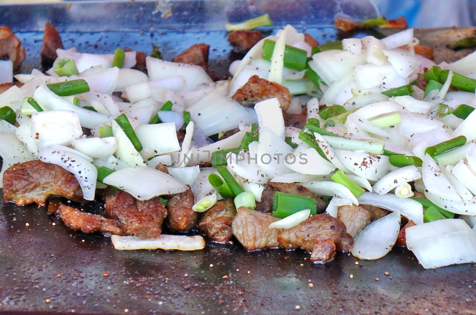 An outdoor vedor cooks meat, onions and leeks on a Teppanyaki griddle
