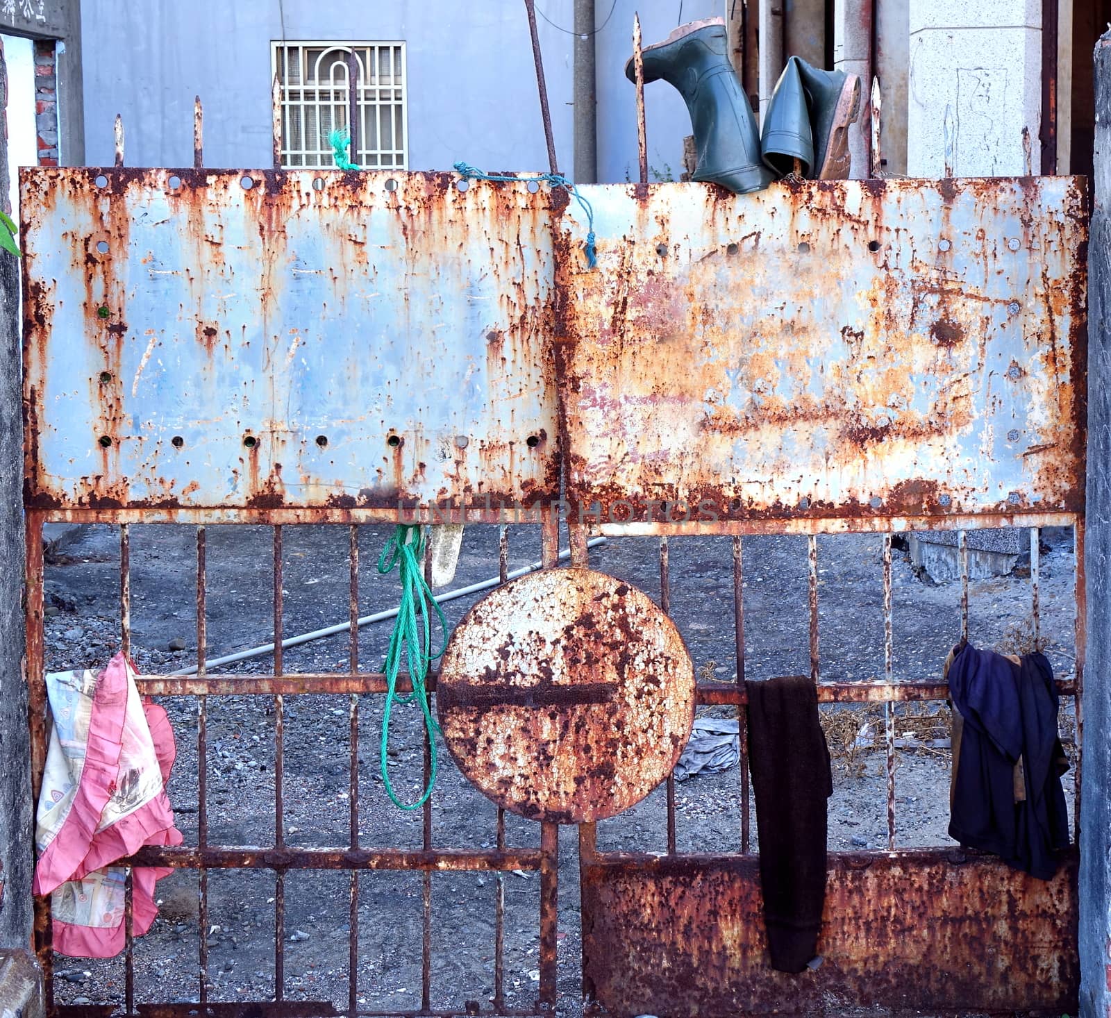 An old rusty iron gate to a deserted house with bits of clothing hanging on it
