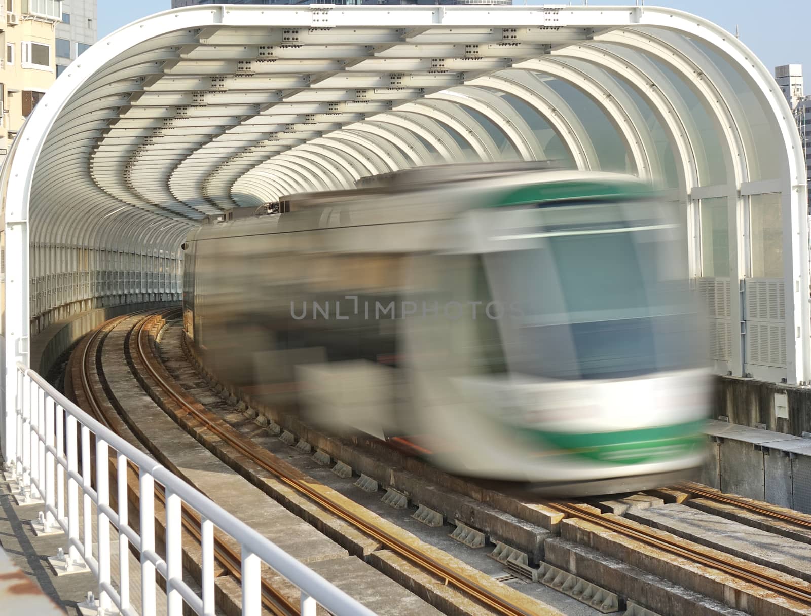 A light rail train emerges from a tunnel with transparent panels