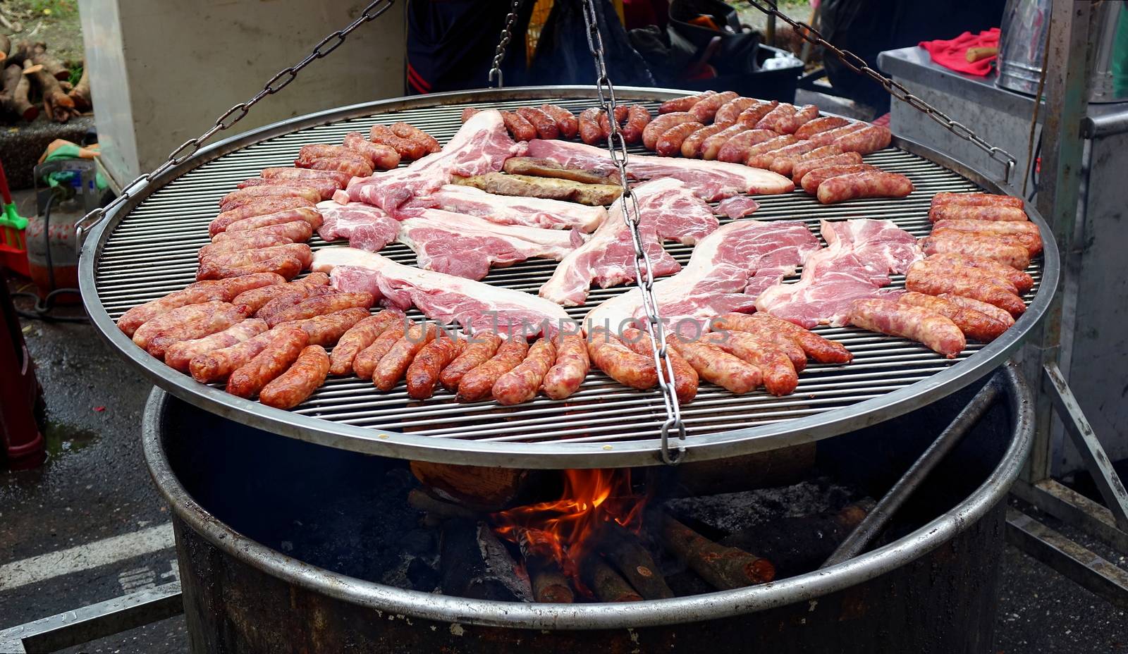A street vendor cooks sausages and slabs of pork on a large barbecue rack