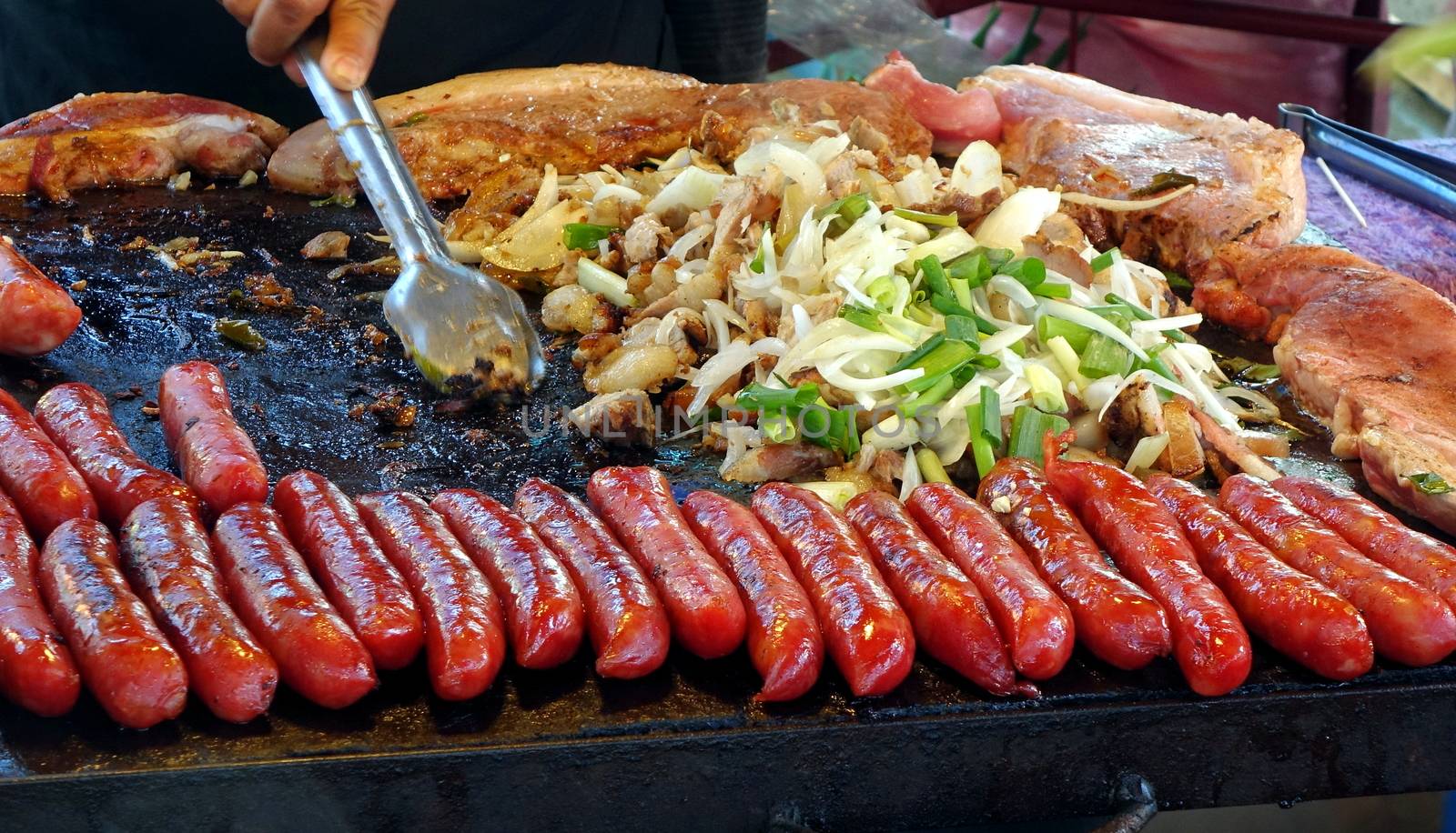 An outdoor vendor cooks sausages, pork and onions
