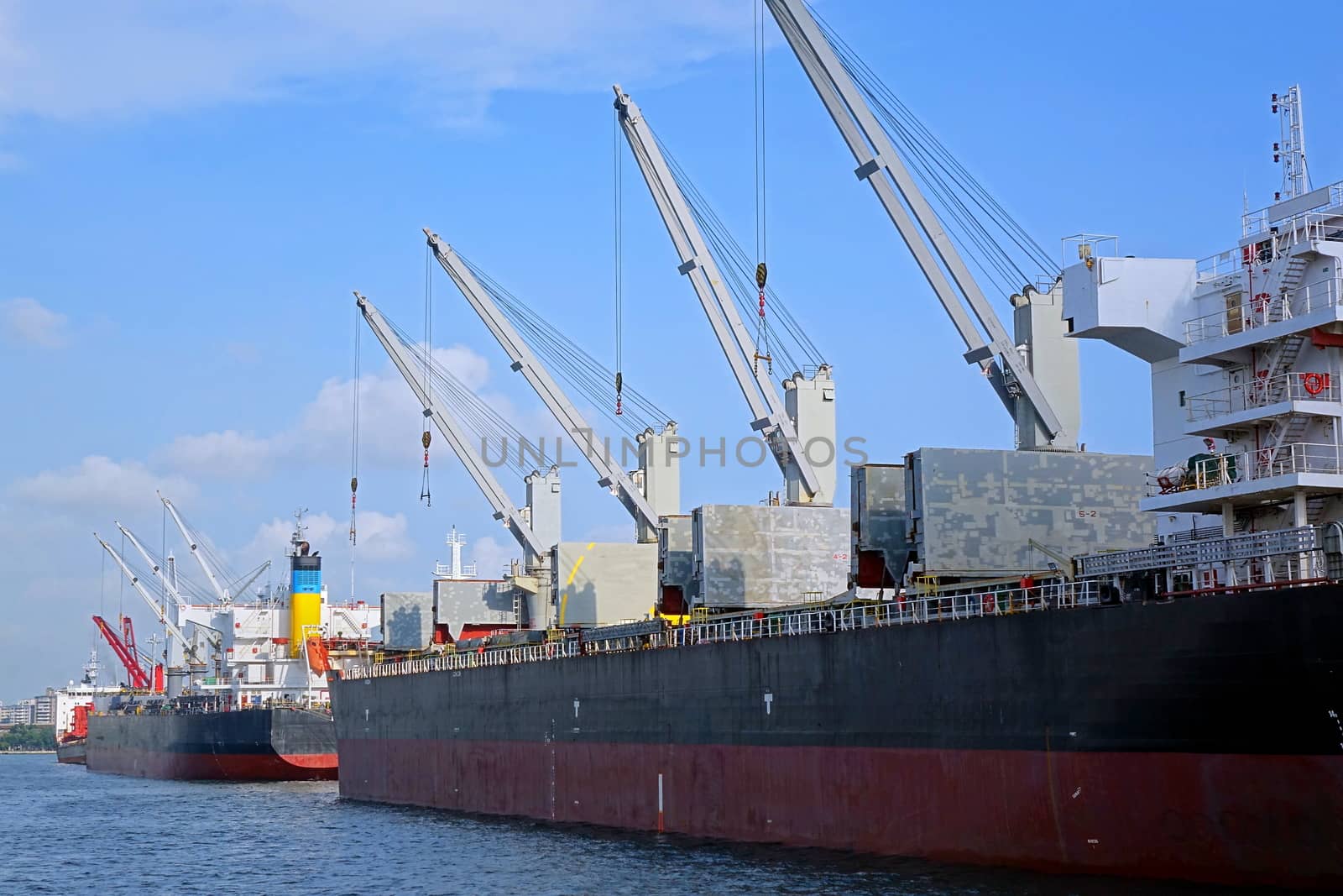 Two large cargo vessels equipped with loading cranes are docked at the harbor
