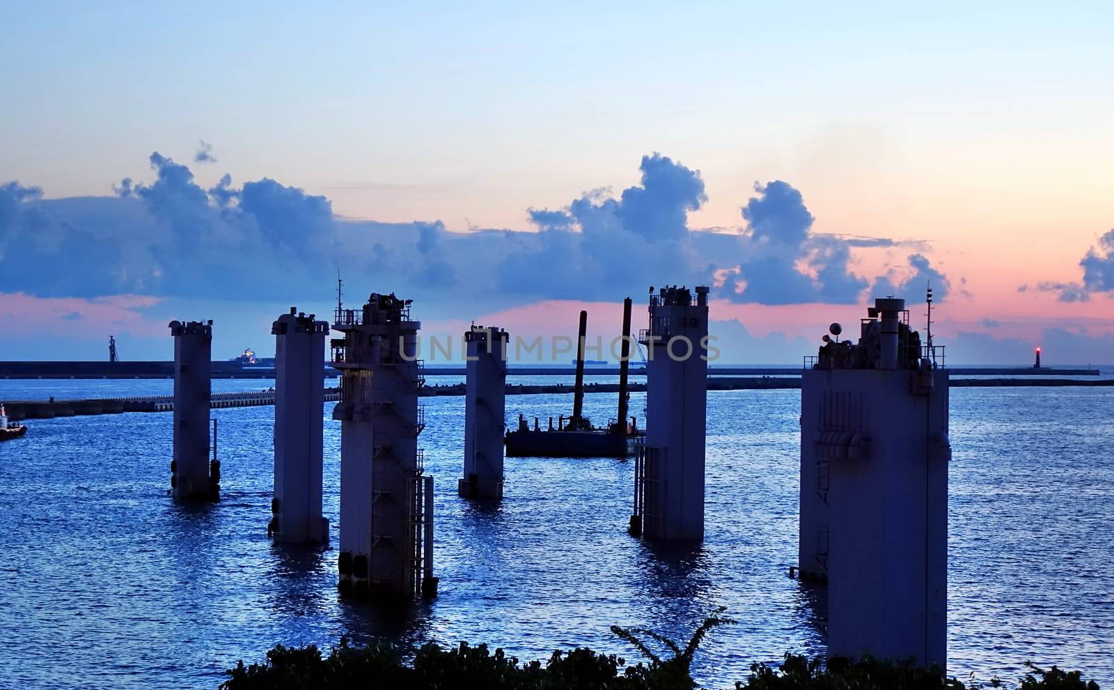 A maritime construction project with large pylons at sunset 
