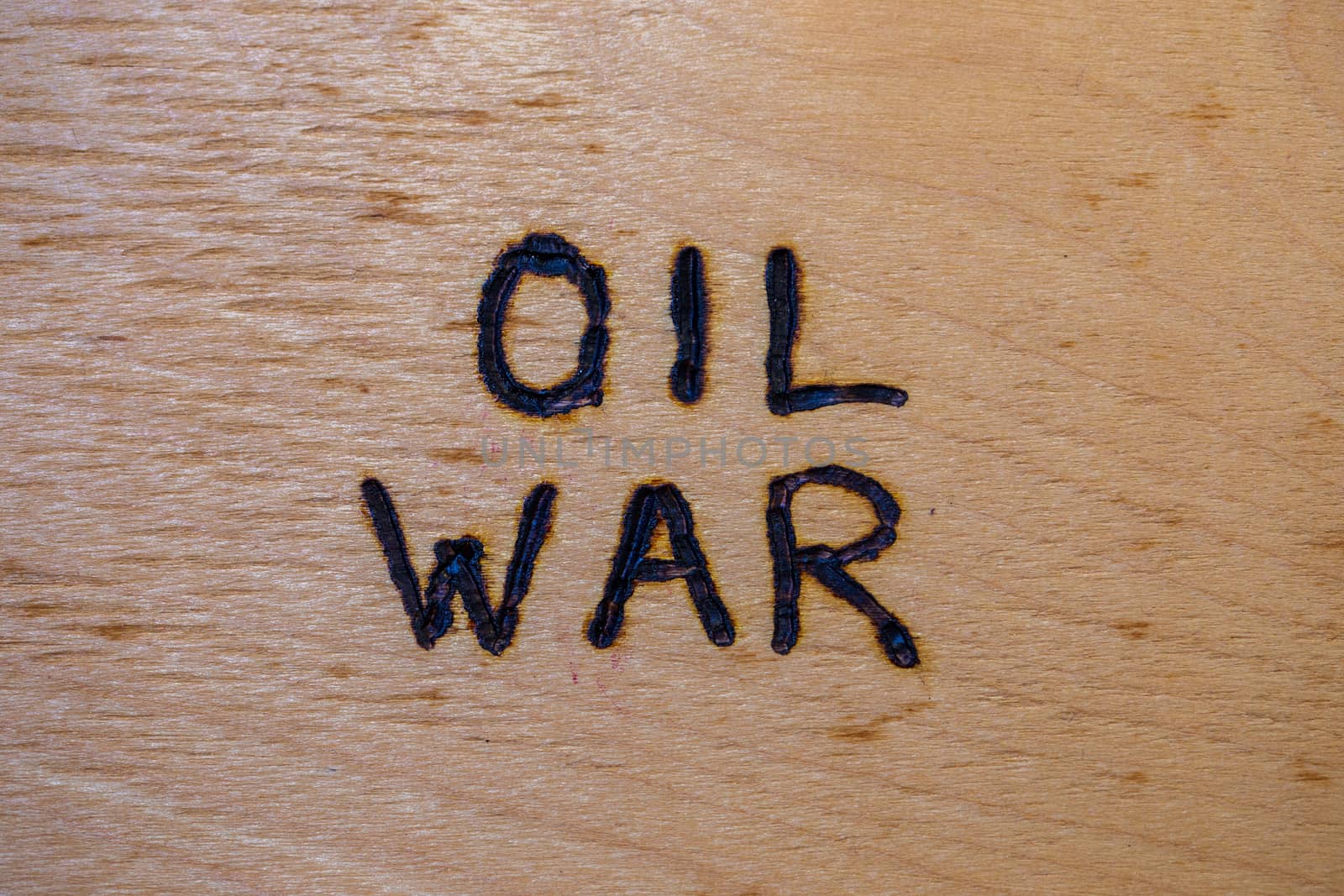the words oil war handwritten on flat bare plywood surface with woodburner.