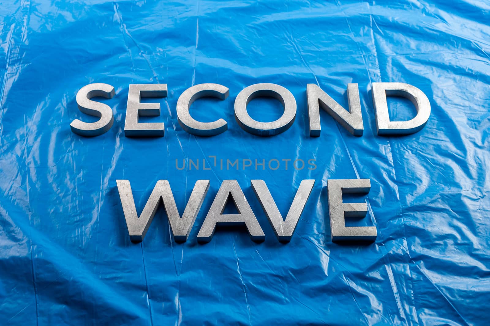 the words second wave laid with silver metal letters over crumpled blue plastic film background in linear perspective.