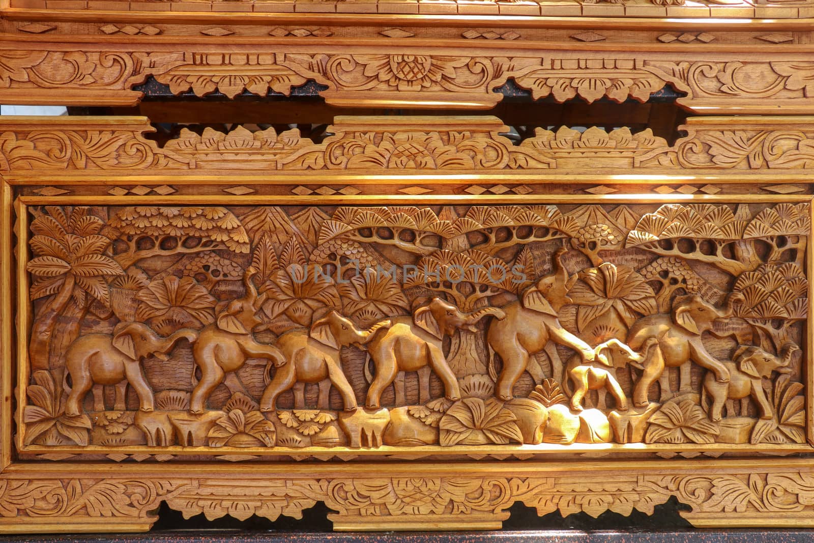 A scene of the last row of elephants in motion carved in wood. Pattern of natural scene. Elephants running through tropical landscape with palm trees in the background. Wood carving decoration. Bali.