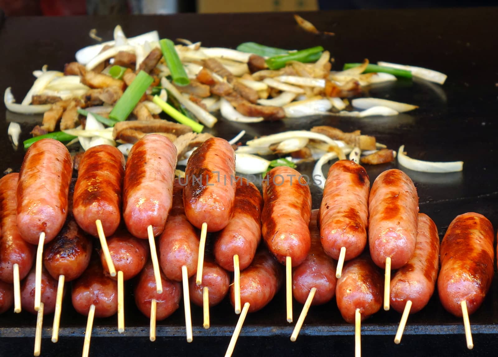 An outdoor vendor roasts fresh sausages and fries pork and leaks