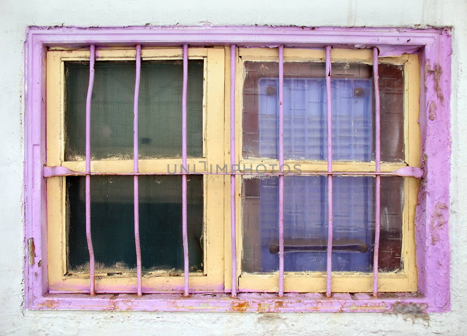 An old window with iron bars and painted in bright pink and yellow colors
