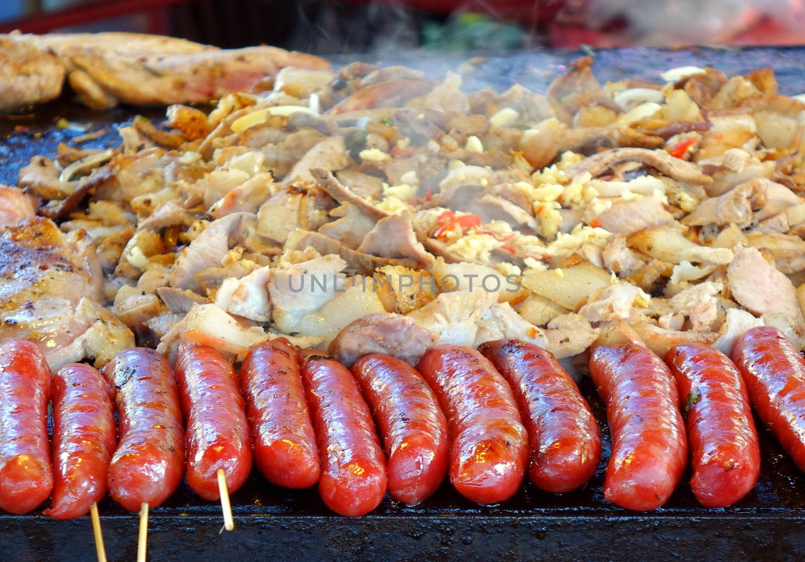An outdoor vedor cooks meat, vegetables and sausages  on a Teppanyaki griddle