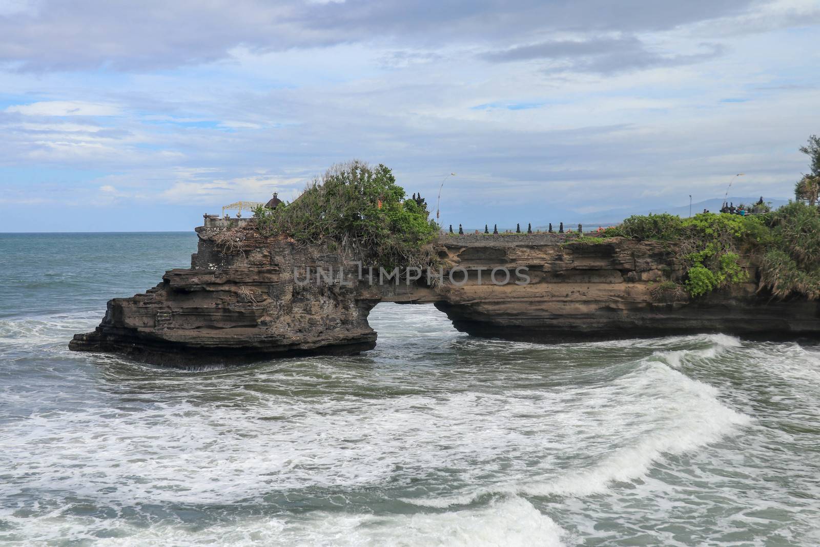 Waves arrive at a rock cliff below Batu Bolong Temple. Tanah Lot temple. Huge hole in rock cliff below Pura Batu Bolong temple. Hindu Temple on the Beatiful Rock in the morning light, Bali, Indonesia.