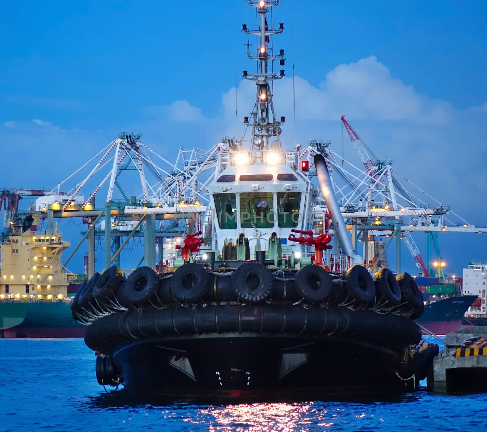 A single tugboat with massive tires fastened to the hull at evening time