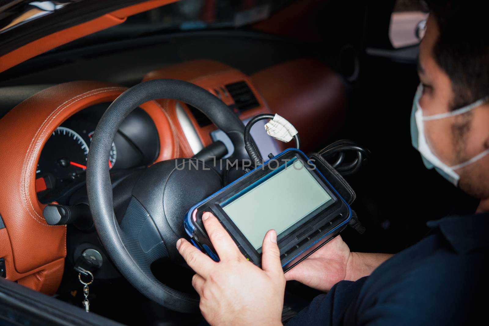 Car mechanic or serviceman checking a car engine by OBD-II electric tools for fix and repair problem at car garage or repair shop