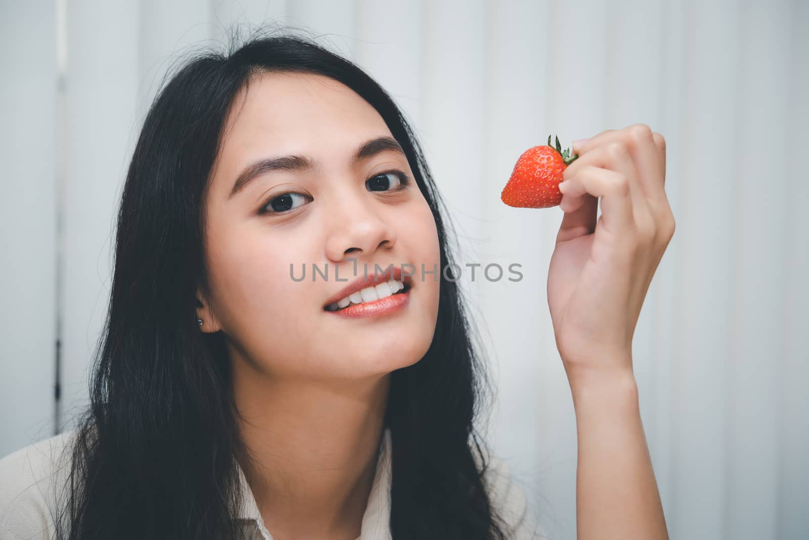 Asian pretty woman holding and eating fresh strawberry is red berry fruit color and sweet juicy with enjoy and happy emotion in concept food, healthy eating in life