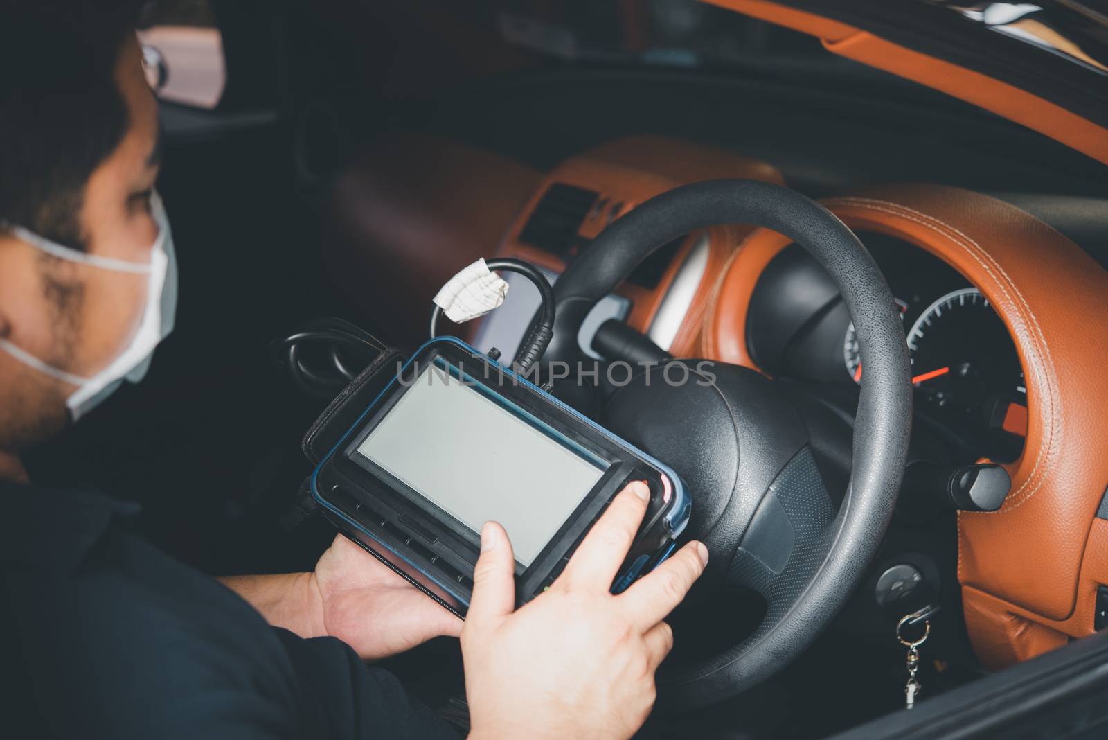 Car mechanic or serviceman checking a car engine by OBD-II electric tools for fix and repair problem at car garage or repair shop