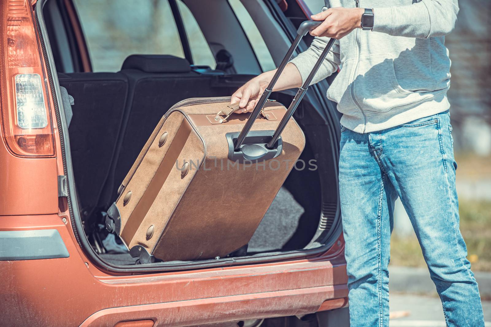 A young man puts luggage in the trunk of a car.