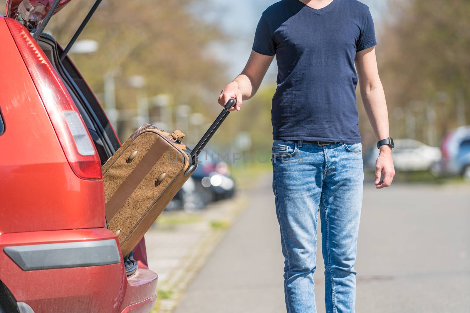 The young man pulls luggage from the car trunk by Edophoto