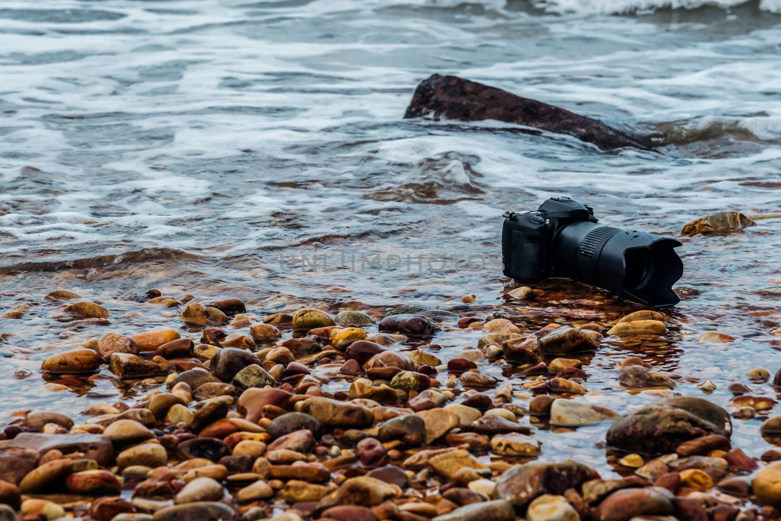 DSLR camera on stone beach wet from water sea wave by PongMoji