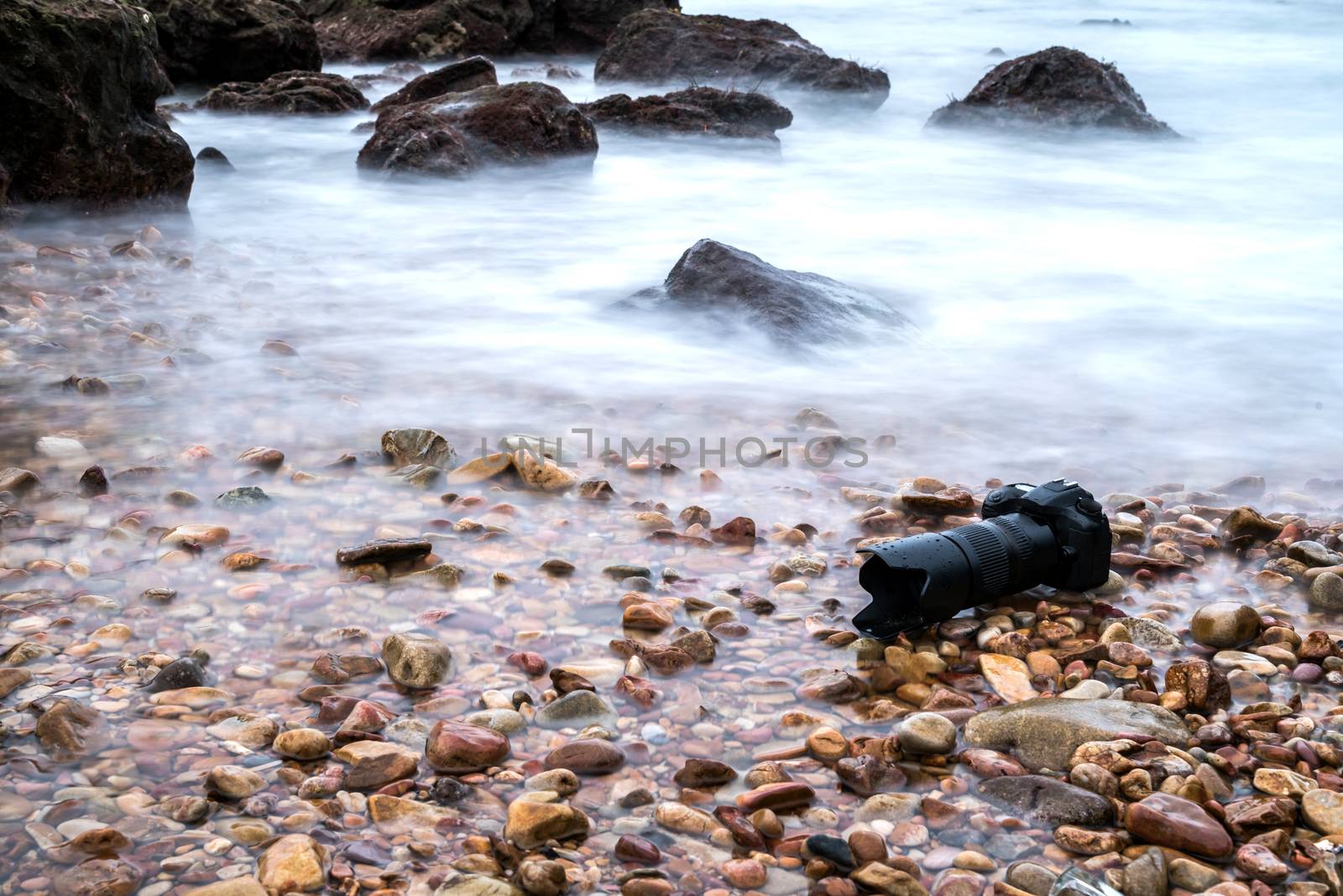 DSLR camera with telephoto lens wet from water sea wave at stone beach when travel and test using in the extreme environment demo waterproof by photographer