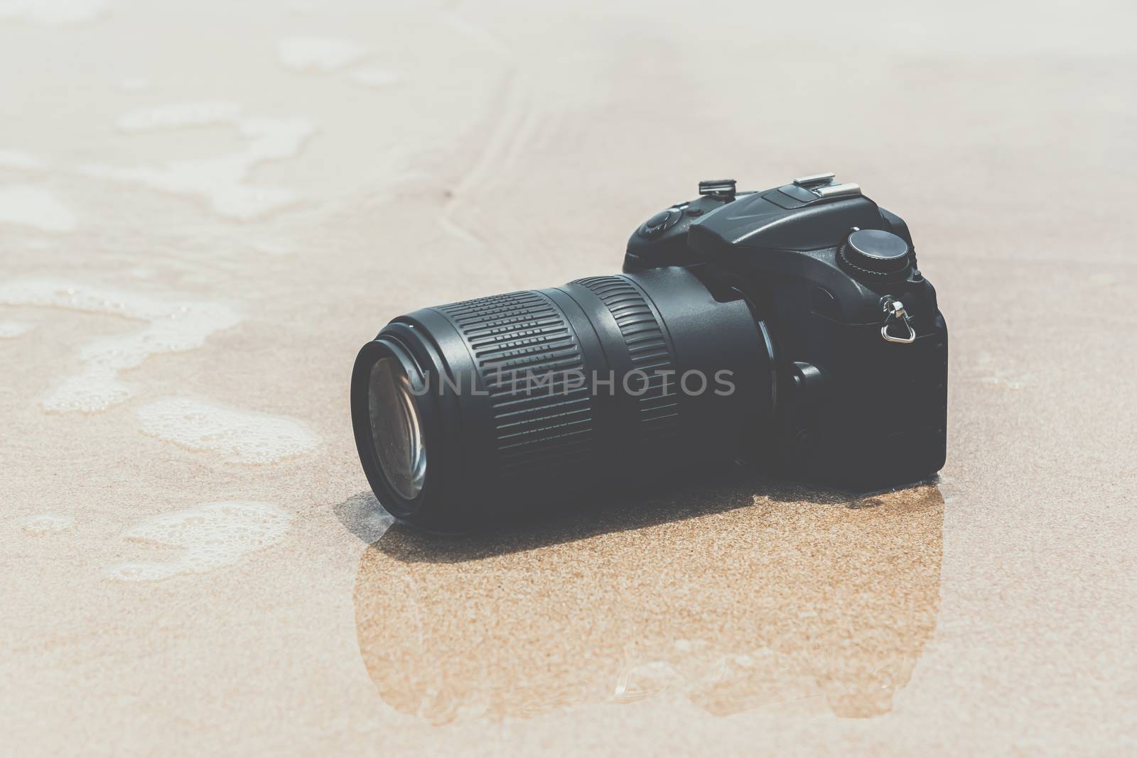 DSLR camera with telephoto lens on a beach it wet from water sea wave when travel and test using in the extreme environment demo waterproof by photographer