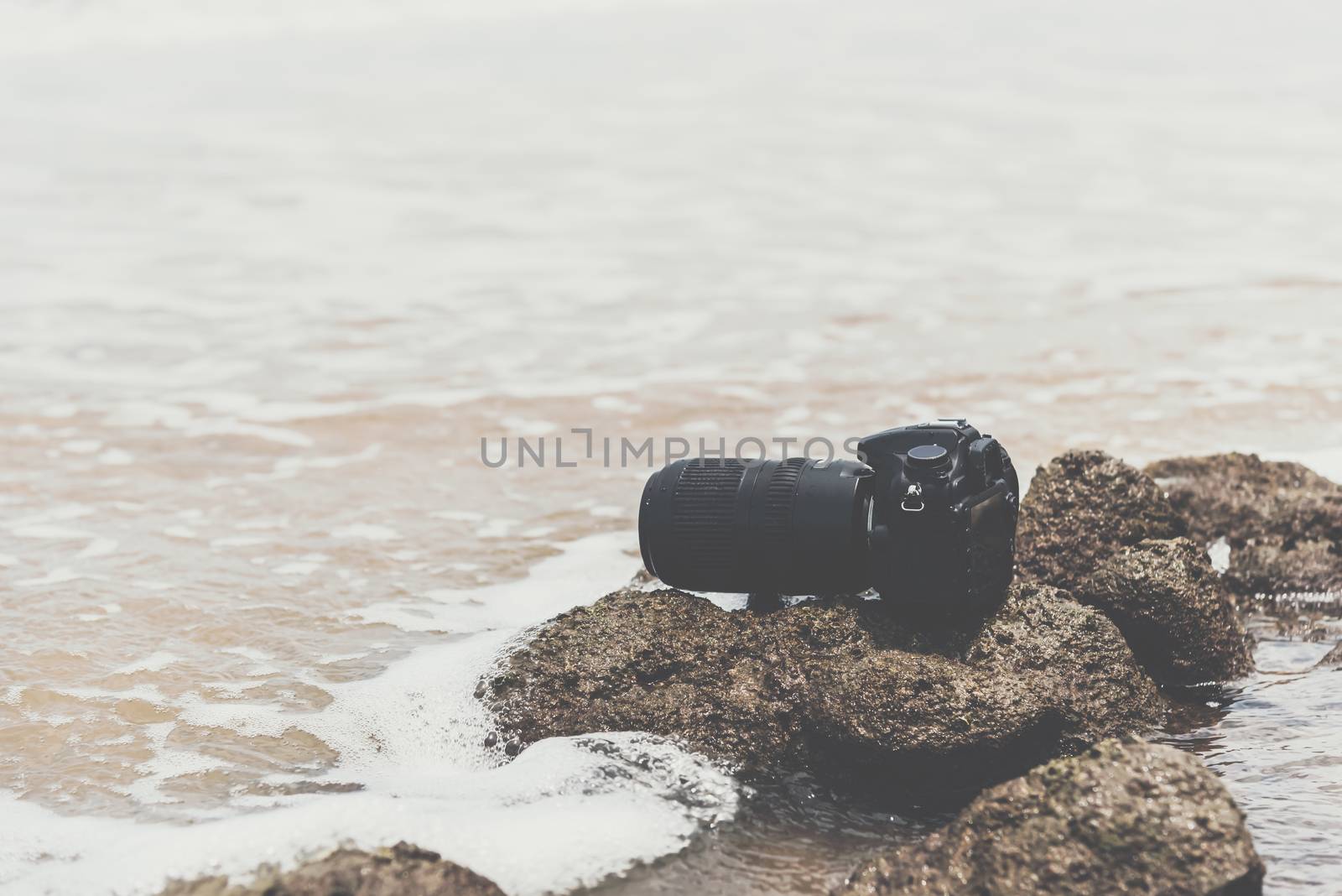 DSLR camera on stone beach wet from water sea wave by PongMoji