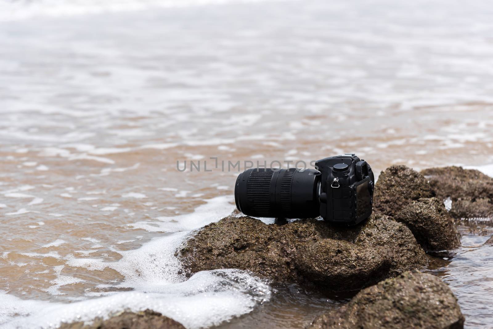 DSLR camera with telephoto lens wet from water sea wave at stone beach when travel and test using in the extreme environment demo waterproof by photographer