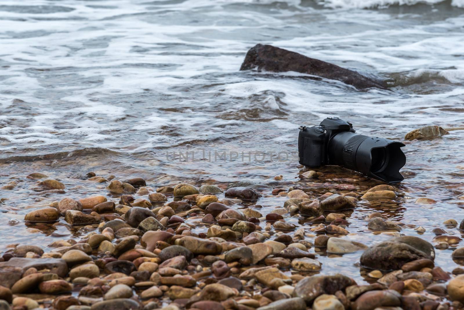 DSLR camera on stone beach wet from water sea wave by PongMoji